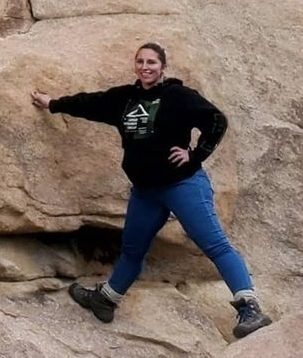 Kaley Nelson in jeans and a sweat shirt leaning against a granite outcrop